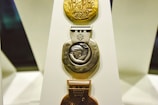 Three Olympic medals displayed vertically on a white stand. The top medal is gold with intricate designs and the Olympic rings. The middle medal is silver, featuring a figure in relief and inscribed with 'Salt Lake 2002' and 'Women's Relay Cross-Country'. The bottom medal is bronze and inscribed with 'Olympic Winter Games'.