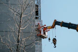 Aerial view of the 26-meter basket crane lifting workers for facade maintenance on a modern building.