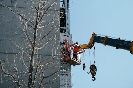 Aerial view of a 26-meter bucket crane lifting workers for facade maintenance on a tall building.