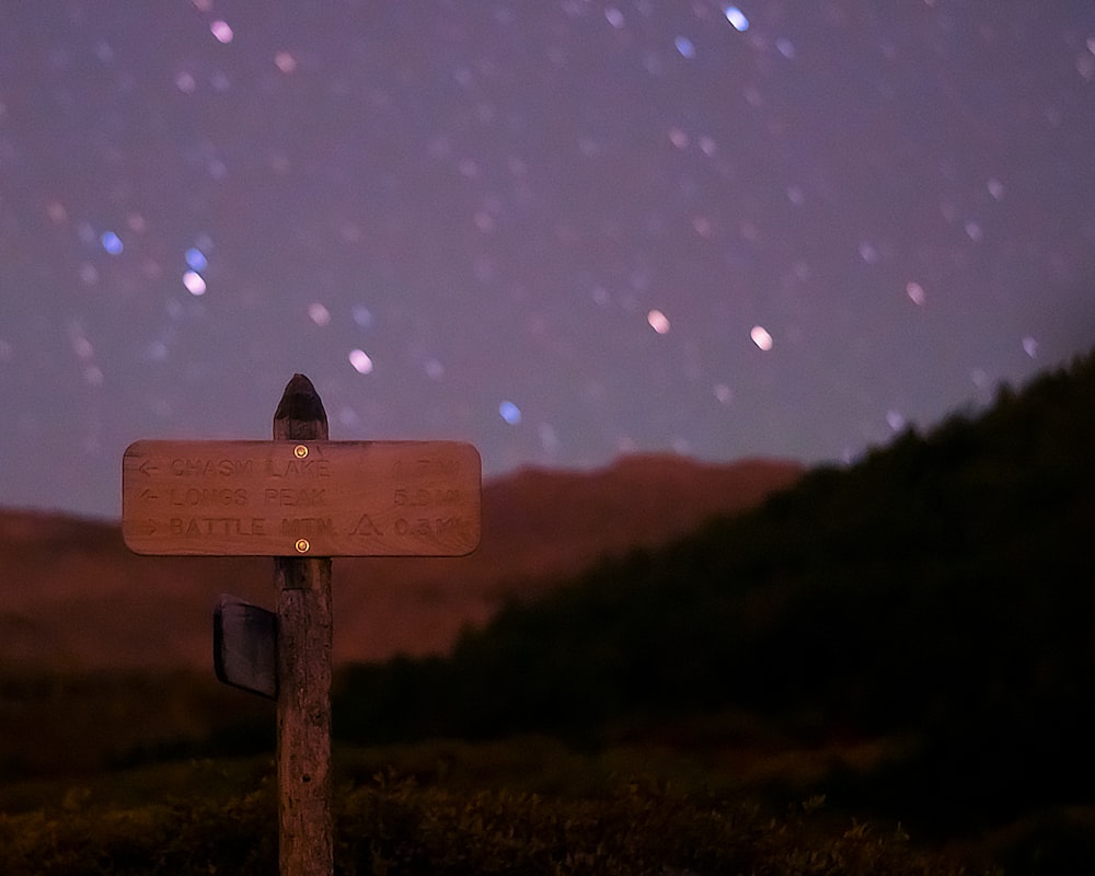 a wooden sign in front of a hill with stars in the sky