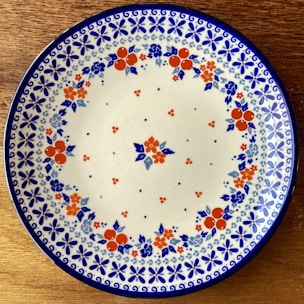 A rustic ceramic plate with a hand-painted floral design resting on a wooden table.