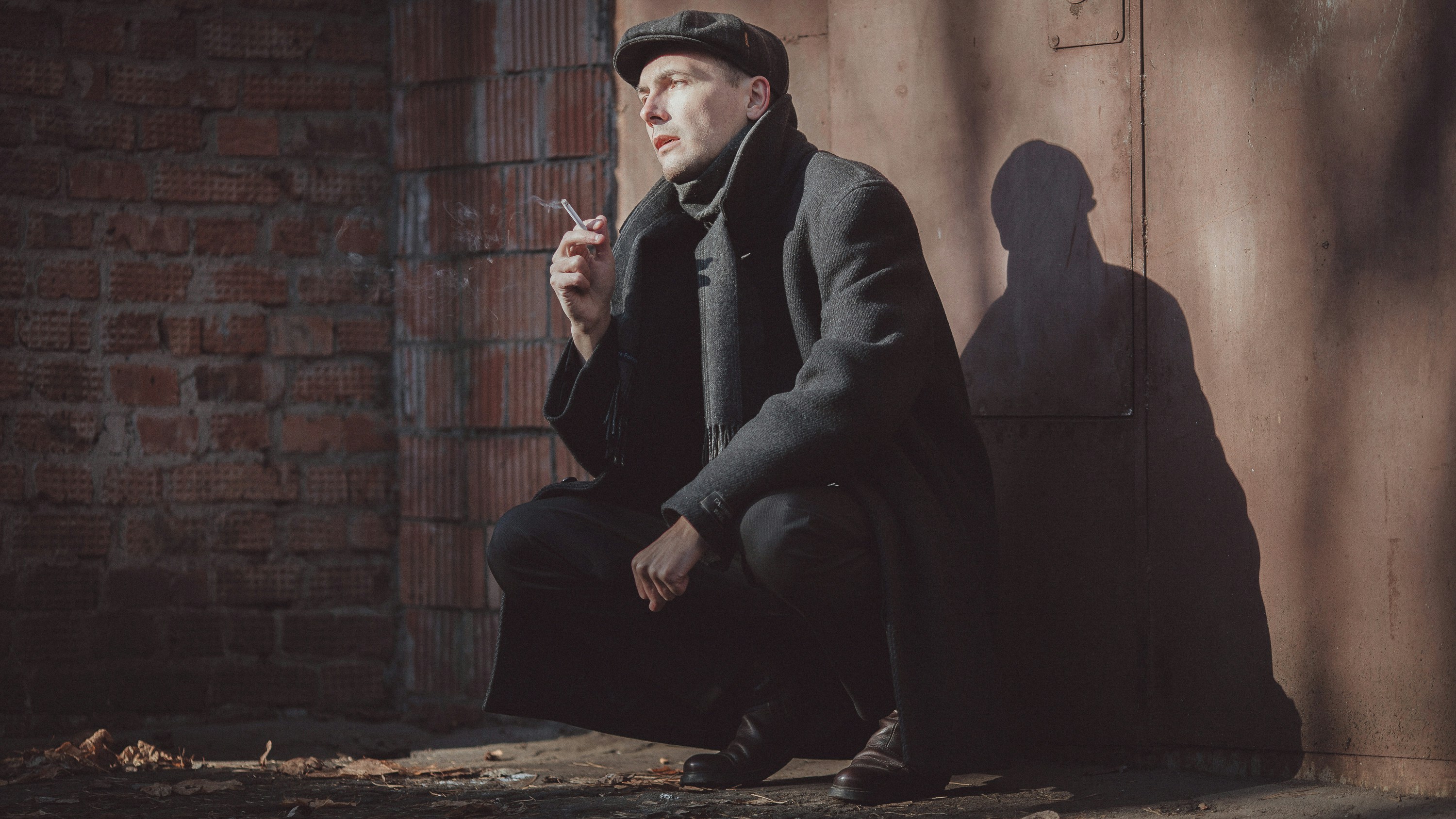 a man squatting down next to a brick wall