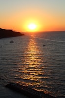 Wide view of the sun setting behind palm trees along the Unawatuna coastline, with fishing boats anchored nearby.