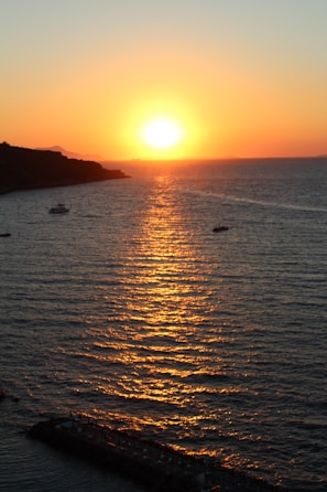 Wide view of the sun setting behind palm trees along the Unawatuna coastline, with fishing boats anchored nearby.