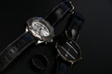 Pair of matching men's and women's watches in black and gold resting on a leather cushion.