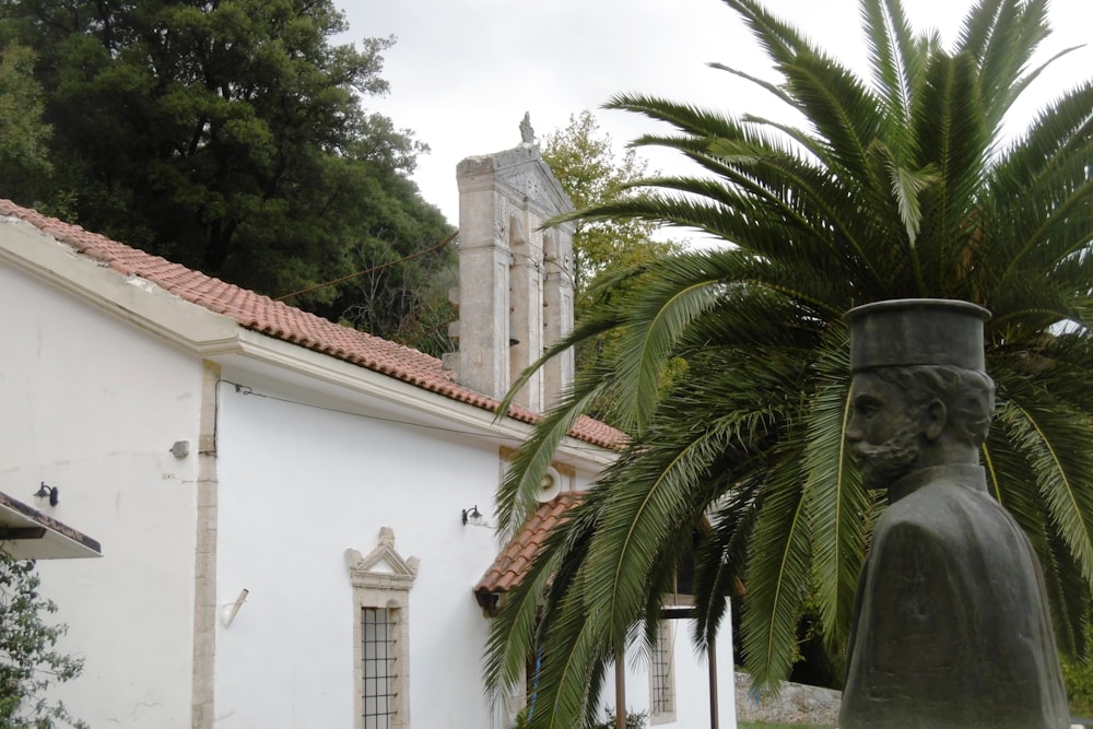 a statue in front of a white building with a tower and a palm tree