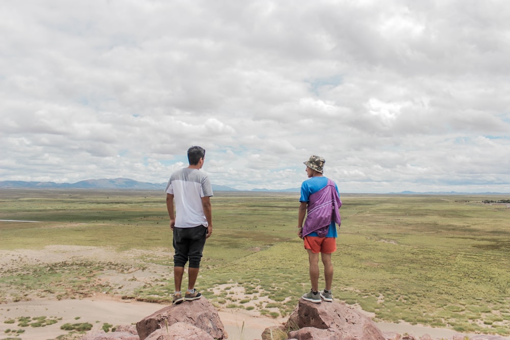 a man and woman standing on a rock overlooking a field