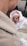 A baby wrapped in warm clothing is being held by an adult. The baby is wearing a pink and white hooded outfit with floral patterns. The adult is dressed in a beige textured jacket. The background includes a paved surface.