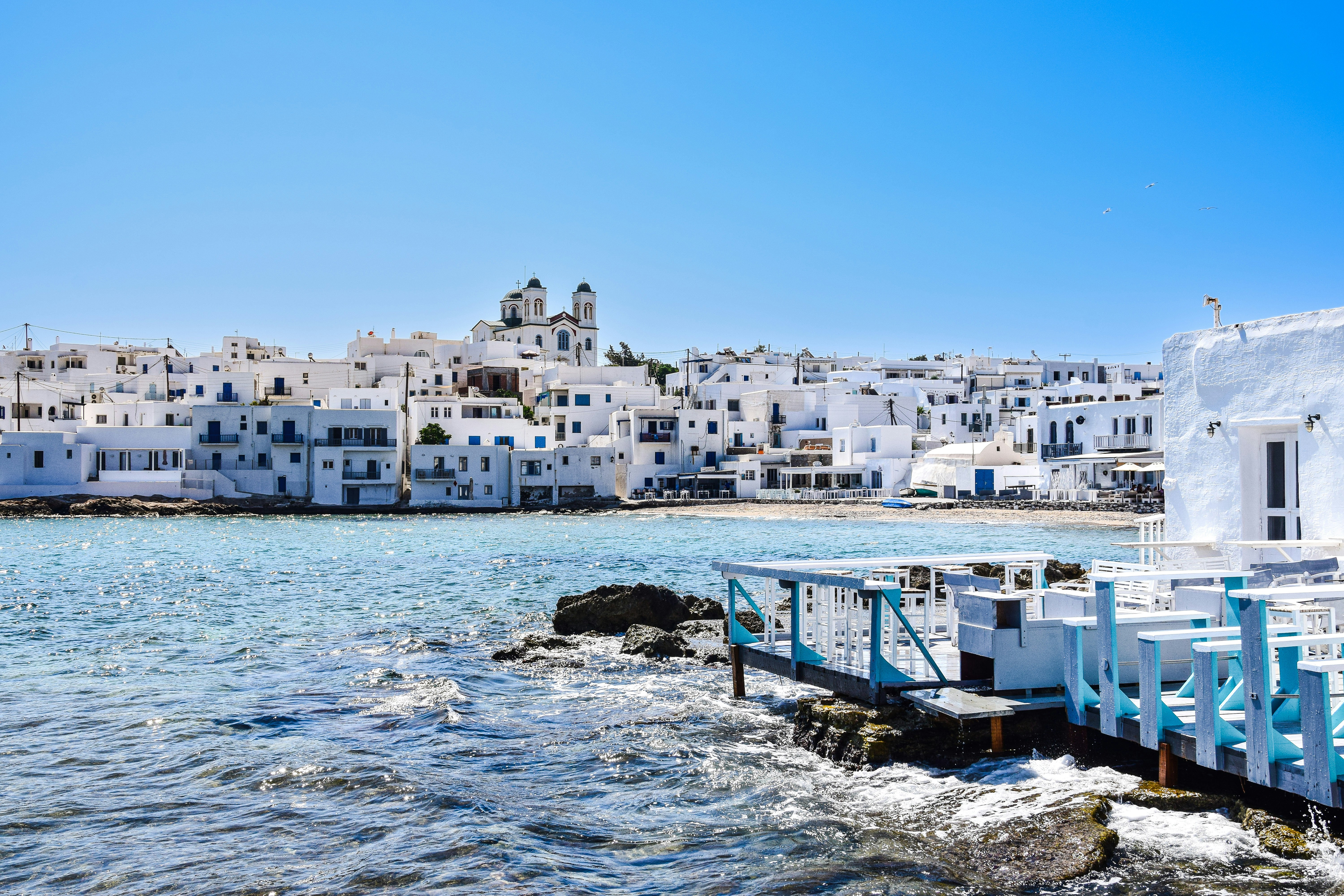a row of white buildings on a rocky shore, Paros, Greece.
