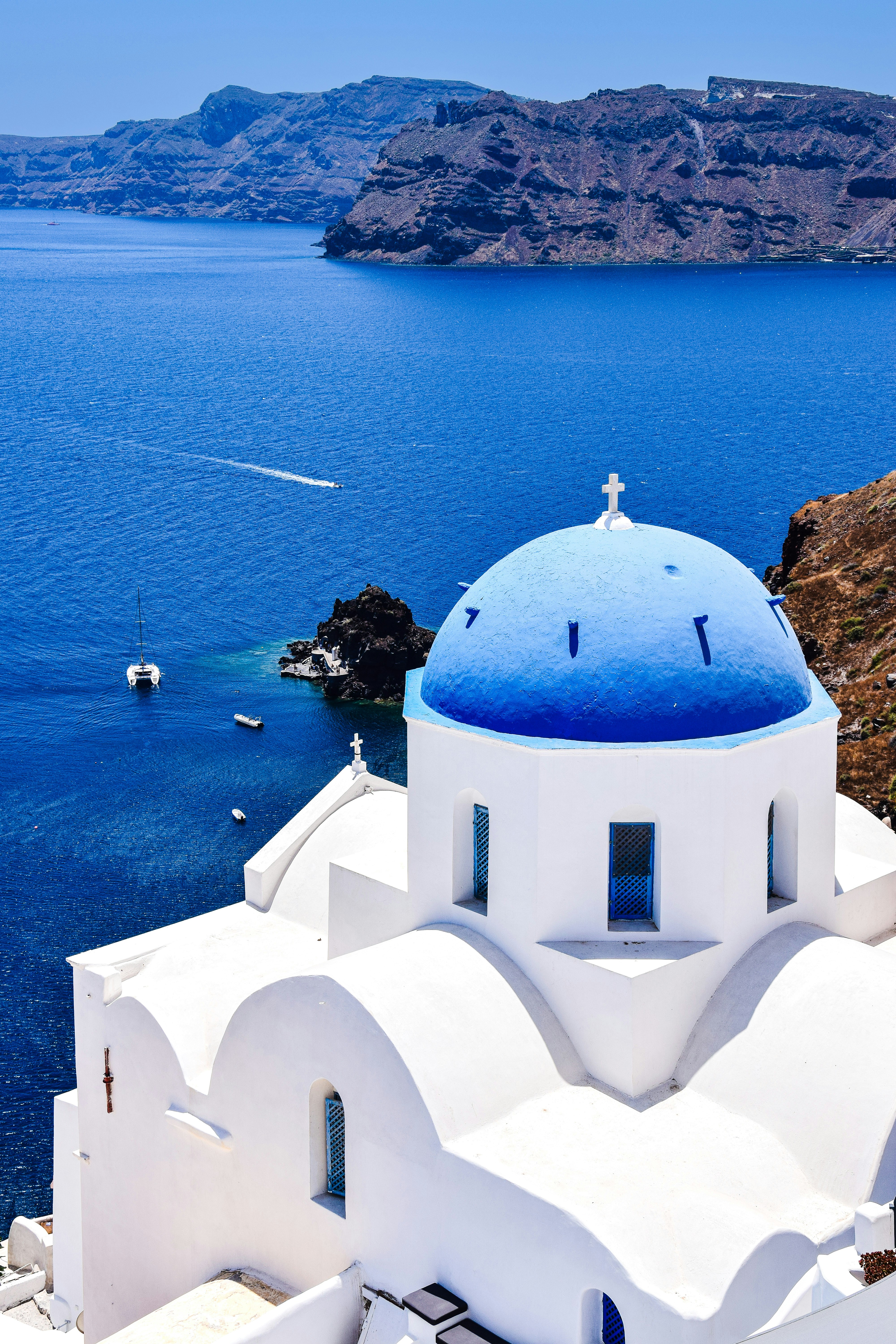 A white building with a blue roof by a body of water with Santorini in ...