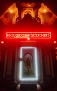 An illuminated shrine with a prominent deity figure surrounded by a bright white light frame. Above the deity is a red neon-lit inscription, with the area cast in a warm, glowing ambience. The setting has intricately designed patterns and pillars, contributing to a sacred and reverent atmosphere.