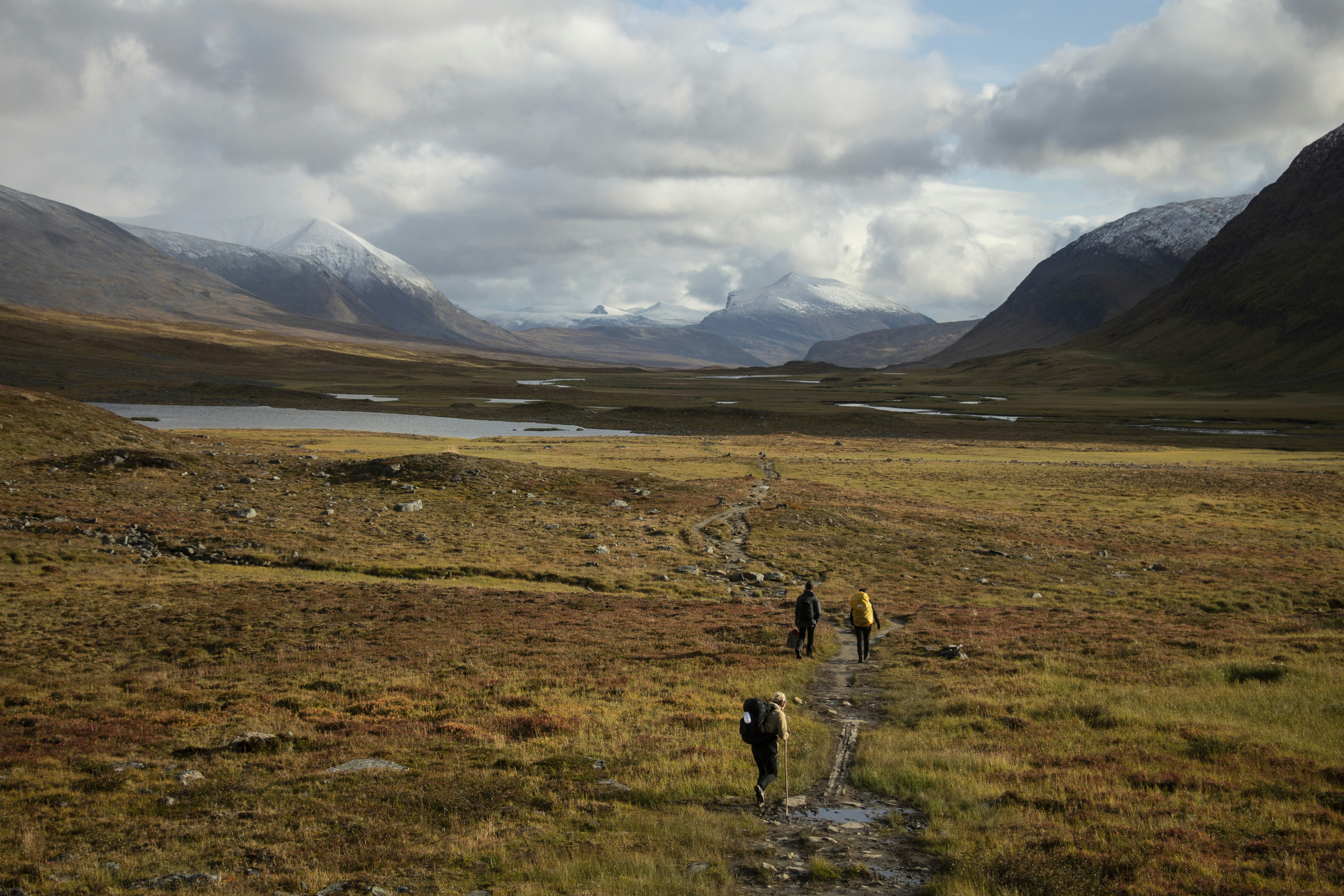 a group of people walking on a trail in a grassy area with mountains in the background, Abisko National Park, Sweden in early Autumn.