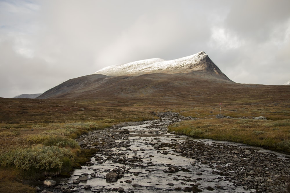 a stream running through a valley with a mountain in the background