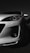 A white car is prominently displayed with a focus on its front headlight and sleek, aerodynamic design. The lighting accentuates the contours and details of the car against a dark background, giving it a dramatic and stylish appearance.