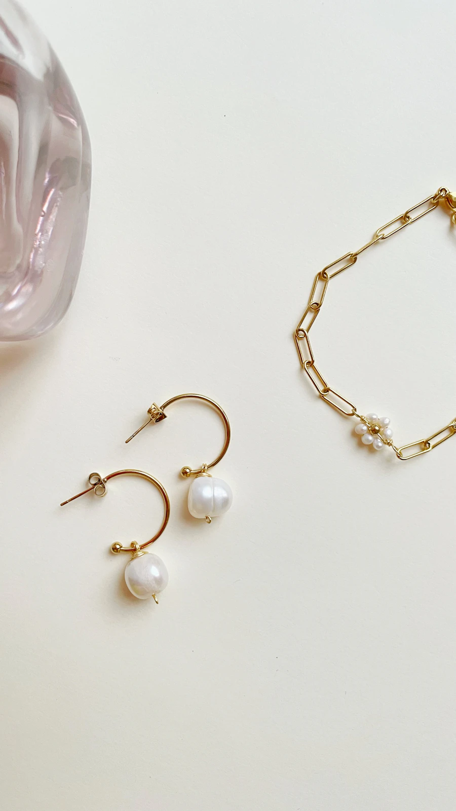 A pair of slim gold hoops, each with a pearl, beside a fine chain