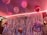 A decorated room features several pink and white balloons with strings, suspended from the ceiling. The background is adorned with metallic silver streamers, creating a shimmering effect. A large inflatable balloon shaped like an engagement ring and a script balloon spell out 'bride to be'. The lighting casts a warm, pinkish glow over the setting.