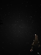 A starry night sky with numerous small white dots scattered across the dark backdrop. In the lower right corner, a large tower-like structure with various antennas and lights is partially visible. The scene suggests a peaceful night environment.