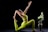 A person in a vibrant green yoga outfit performs a yoga pose, reaching one arm upward and holding a foot with the other. Next to them is a decorative vase with large white flowers and green leaves, set against a stark black background.