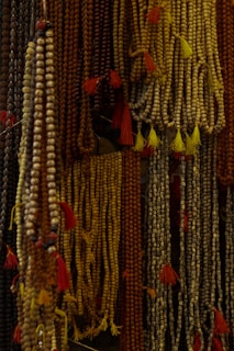 Numerous strands of prayer beads hang in clusters, featuring earthy tones and intricate, small round beads with tassels attached to them.