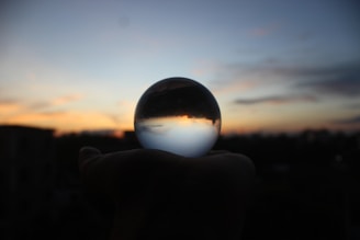 Close-up of a hand holding an obsidian mirror reflecting a sunset sky.