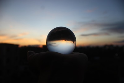 Close-up of a hand holding an obsidian mirror reflecting a sunset sky.