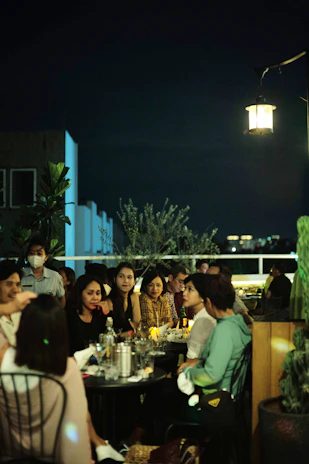 An intimate rooftop dining scene with a group of black adults enjoying an upscale chef’s table experience at sunset.