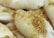 Close-up view of dumplings with a golden brown topping, possibly garlic or onions, glistening with oil or sauce. The dumplings appear soft and slightly glossy.