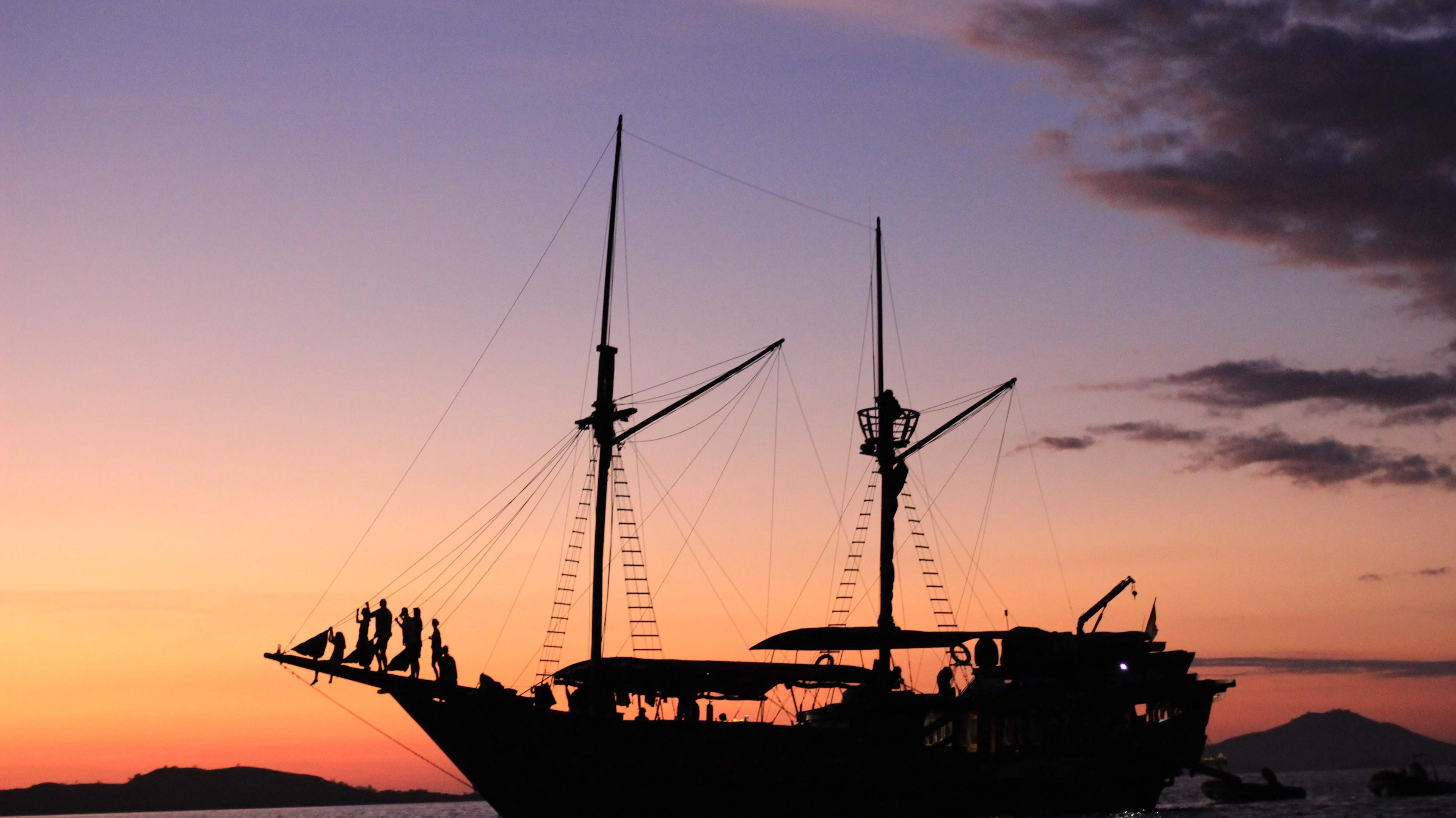 A phinisi sailing boat silhouetted at sunset off Kalong Island, near Labuan Bajo