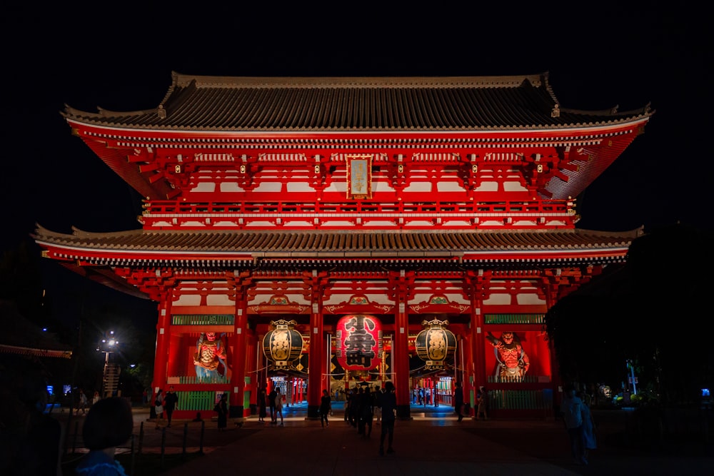 a red asian building with a large archway and people walking around