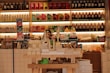 A well-stocked shop shelf filled with various beauty and wellness products, including bottles, boxes, and jars. The shelves are neatly organized with different color-coded sections containing skincare bottles, soaps, and colorful packaging. The lighting is warm and inviting.