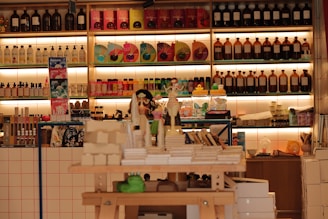 A well-stocked shop shelf filled with various beauty and wellness products, including bottles, boxes, and jars. The shelves are neatly organized with different color-coded sections containing skincare bottles, soaps, and colorful packaging. The lighting is warm and inviting.