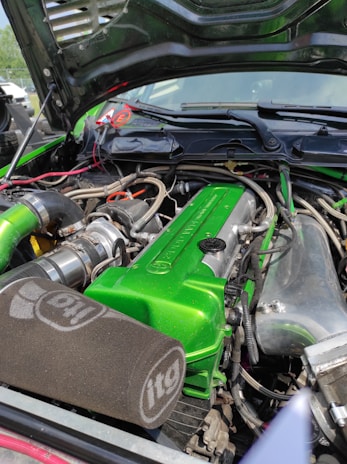 A car engine with a vibrant green valve cover and various components, including hoses and wires. The engine bay has a large, black itg air filter and shiny metallic parts. The hood is open, revealing a clean and well-organized setup.