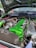 A car engine with a vibrant green valve cover and various components, including hoses and wires. The engine bay has a large, black itg air filter and shiny metallic parts. The hood is open, revealing a clean and well-organized setup.