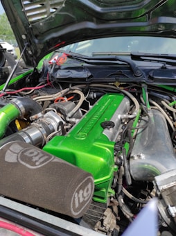A car engine with a vibrant green valve cover and various components, including hoses and wires. The engine bay has a large, black itg air filter and shiny metallic parts. The hood is open, revealing a clean and well-organized setup.