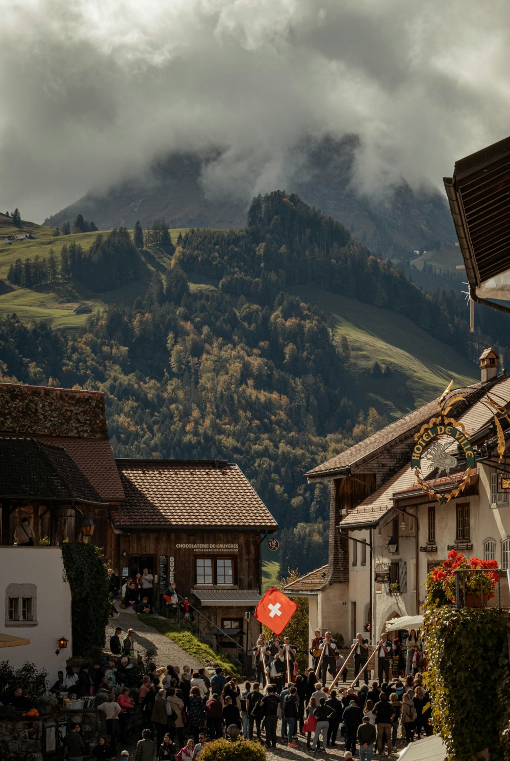 a group of people walking on a street with buildings and mountains in the background