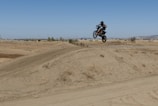 A motocross rider mid-air over a dirt track under a bright Florida sky.