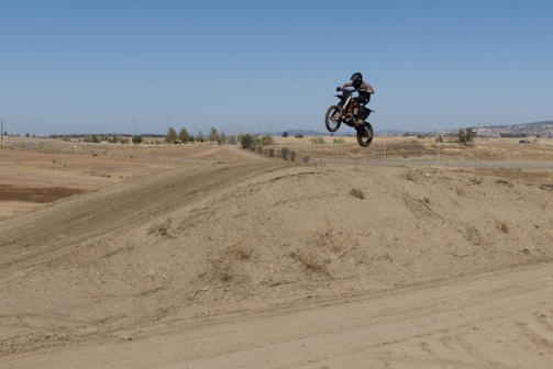 A motocross rider mid-air over a dirt track under a bright Florida sky.