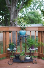 A handmade clay plant stand holding vibrant potted plants, placed on a wooden deck.