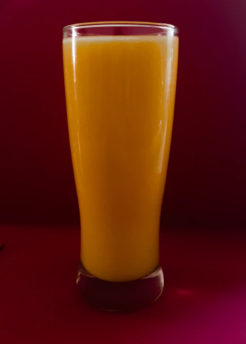 Close-up of a vibrant orange juice being poured into a glass with fresh oranges in the background