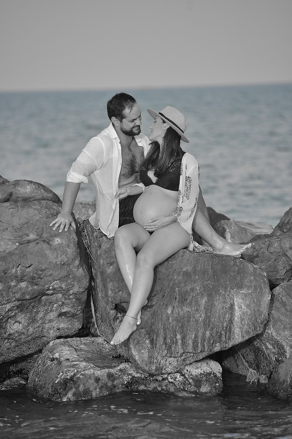 a man and woman sitting on a rock by the water