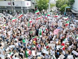 A peaceful protest with people waving the Iran Lion flag under a clear sky.