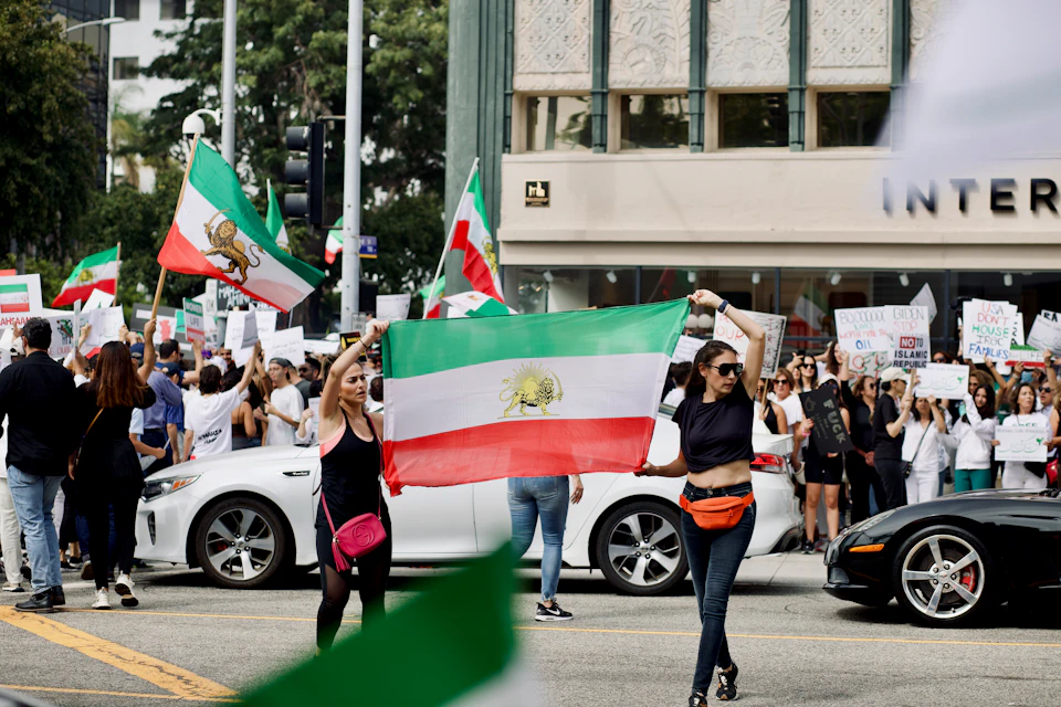 Two women hold up a large flag with green, white, and red colors together