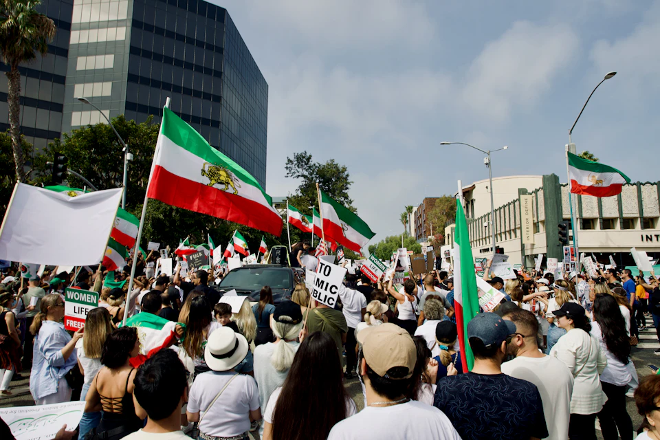 The image captures a large crowd of people gathered on a street, holding up various signs and banners with messages such as "To Mic!" and "Women's Rights". The crowd is diverse, consisting of individuals from different age groups and genders, all united in their cause. Some are standing close together while others maintain some distance, creating a sense of community among the protesters. In the background, there are buildings that add context to the urban setting where this demonstration is taking place.