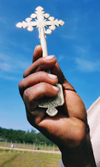 Hands holding a cross pendant against a blue sky background