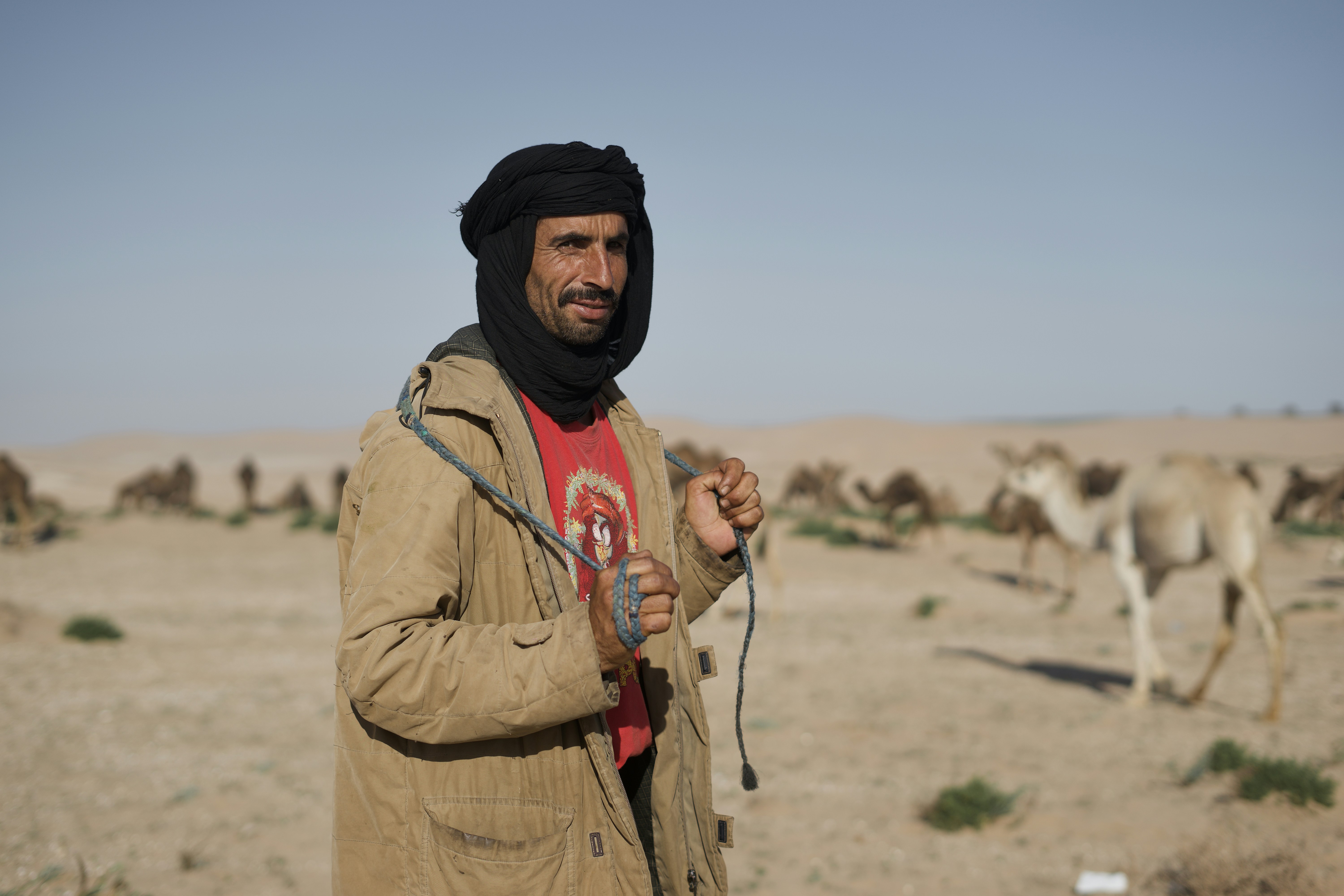 A man with a scarf on his head and a group of animals in the background