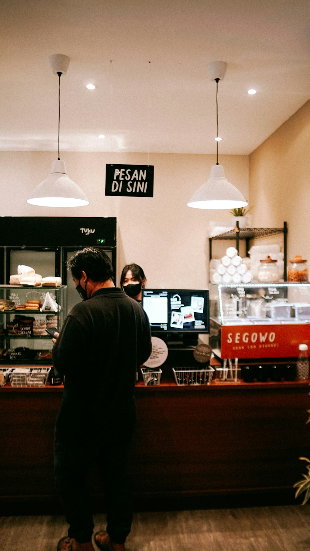 a man and woman standing in front of a counter with a television and a sign