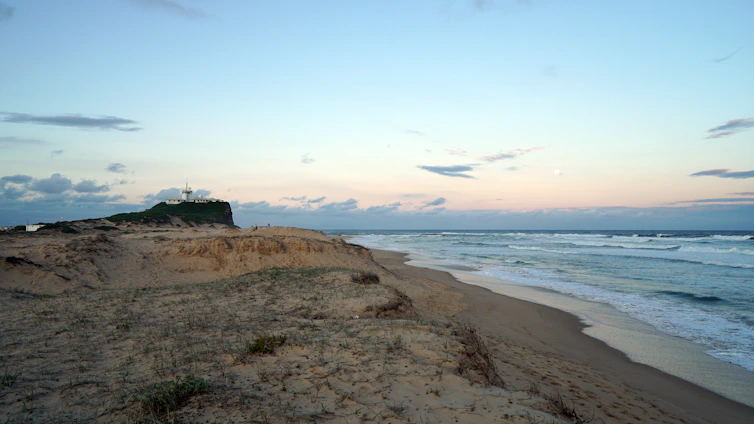 A serene Scandinavian coastline at dawn, with soft sand dunes meeting a calm ocean under a pale ivory sky.