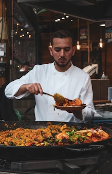 Portrait of Alberto de Lopez Muñoz in a lab coat holding a paella pan, with a backdrop of scientific equipment and Spanish flags.