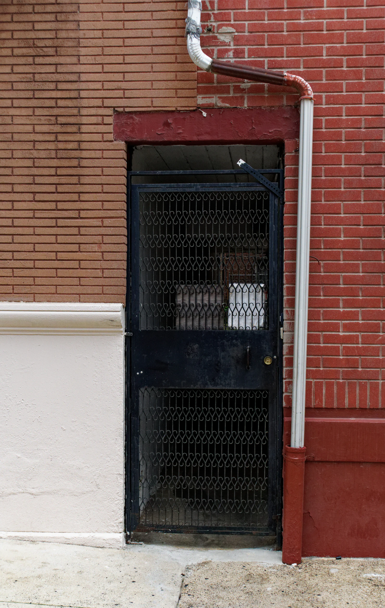 White downspout on a brick exterior wall terminating into underground drain piping at grade