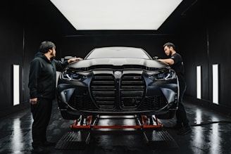 a couple of men standing next to a car in a garage